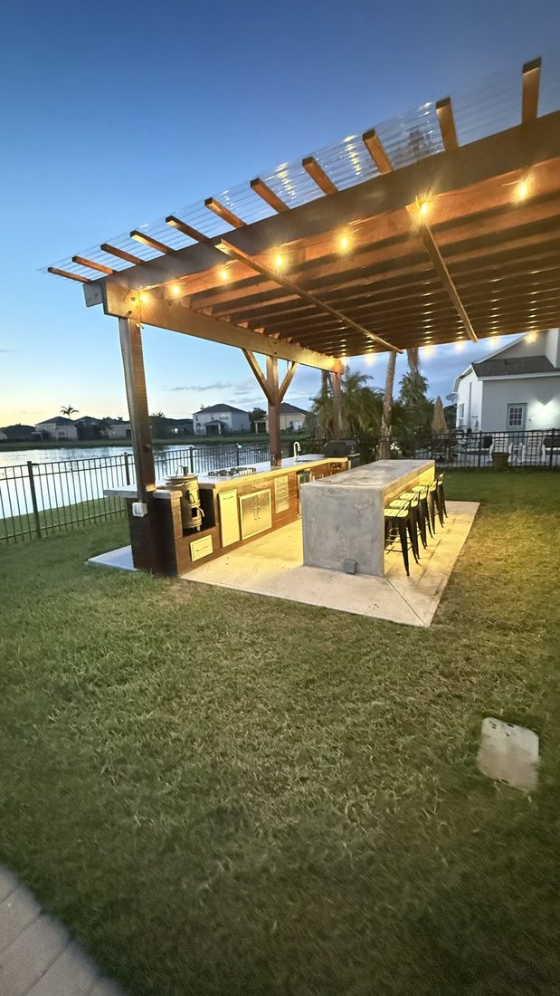 Waterfront pergola with an outdoor bar, seating, and string lighting at dusk